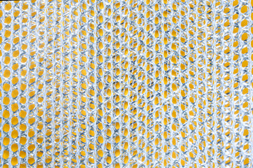 Close-up macro of a metallic dishwashing sponge showing interwoven silver mesh forming honeycomb-like cells against a yellow background. Photo. High resolution