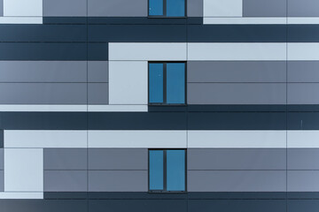 Detailed view of a modern house facade with gray and white surfaces. Three windows stand out against the strict geometry