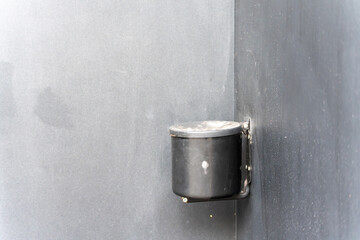 A black wall-mounted ashtray is attached to a gray wall. The close-up shows the simple design for public smoking areas.