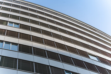 A modern office building with a curved facade and numerous windows and louvers. The image emphasizes the architectural dynamism.