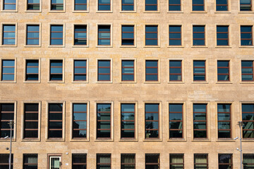 Facade of an office building with regularly arranged windows made of yellowish sandstone. The strict grid structure conveys order and functionality.
