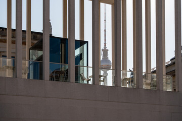 View through concrete struts onto a terrace with tables, with the Berlin TV Tower in the background. Urban design meets iconic landmark.