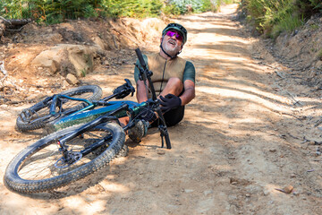 Senior cyclist touching his injured ankle after falling with his e-bike on a mountain trail