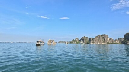 A panoramic view of majestic limestone islands rising from the calm emerald waters of Ha Long Bay, Vietnam, under a clear blue sky. Panning footage.