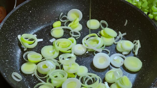 Adding olive oil to sliced leeks that are frying in a pan.