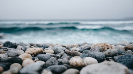 Serene rocky shoreline with smooth pebbles and crashing ocean waves under a stormy sky.