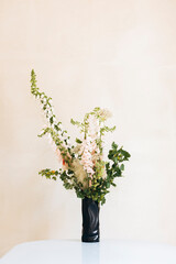 Minimalist floral arrangement with foxgloves in black vase on light table.