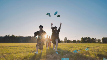 Happy graduates in caps and gowns toss diplomas in the air, celebrating their graduation at sunset...