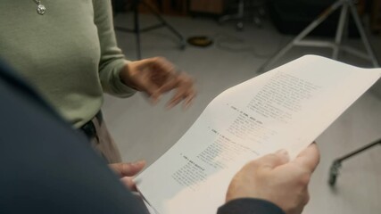 Over the shoulder shot of unrecognizable filming director holding paper script and reading it together with African American actress