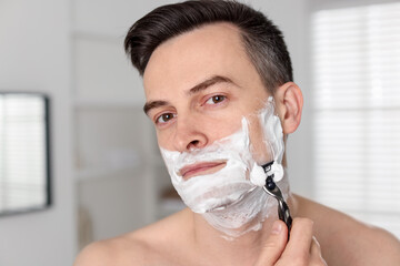 Handsome man shaving with razor at home