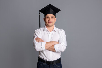 Student with crossed arms after graduation on grey background