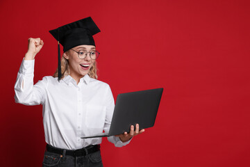 Happy student with laptop after graduation on red background. Space for text
