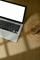 Overhead view of laptop with blank screen and coffee cup on wooden table in morning sunlight