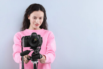 Woman with professional video camera on light grey background, selective focus. Space for text