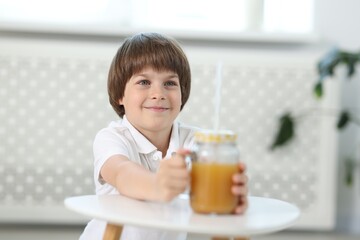 Little boy with mason jar of orange juice at table indoors, selective focus. Refreshing drink
