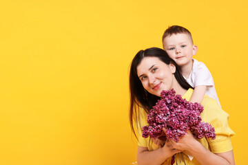 Mother and her son with bouquet of lilac flowers on yellow background, space for text