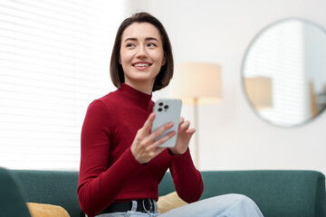 Fototapeta premium Woman using modern smartphone on sofa at home