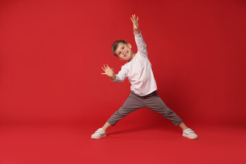 Happy little boy dancing on red background, space for text