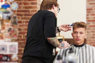Professional barber cutting client's hair with scissors in barbershop