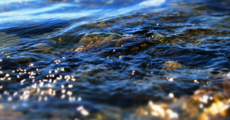 Cristal river, waterfall glowing water background, stones, rapids and boulders. Texture clear cold sea water with reflection sunlight. Falling and flowing water. Scenery lake. Shallow DOF