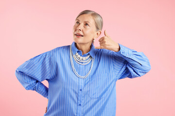 Senior woman wearing elegant pearl jewelry on pink background