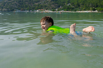 Small child swimming in life jacket in shallow water. Summer vacation. Safety of child while swimming outdoors