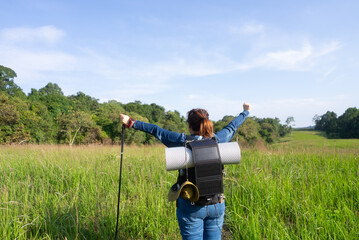 Rear view of an Asian woman with a solar-powered backpack raising her arms, symbolizing sustainable hiking, off-grid adventure, and eco-friendly travel in nature.