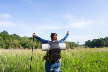 Rear view of an Asian woman with a solar-powered backpack raising her arms, symbolizing sustainable hiking, off-grid adventure, and eco-friendly travel in nature.