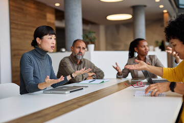 A group of businesspeople are gathered around a table, discussing something. Scene is serious and...