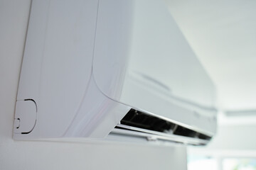 Close-up view of modern air conditioning unit mounted on white wall in bright room. Home cooling...