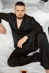 A man in black silk pajamas is sitting in bed 