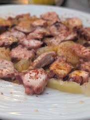 Close-up of traditional Spanish dish Galician-style octopus served on a wooden plate with paprika, olive oil, and sea salt. Rustic and authentic seafood presentation