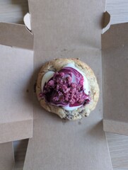Close-up of a big chocolate chip cookie topped with creamy cream cheese and fresh raspberries
