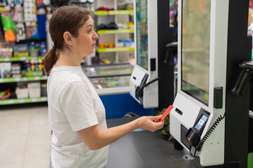 Woman paying with credit card at self-checkout. 