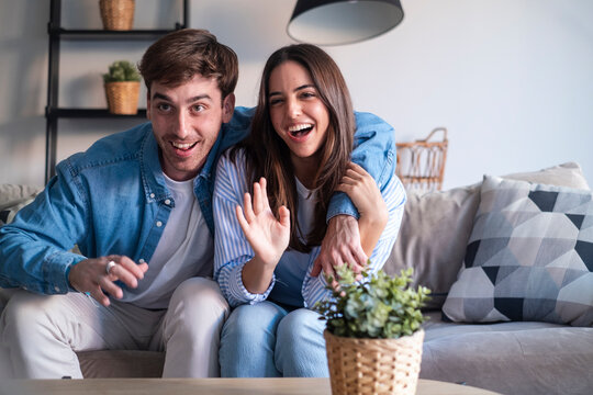 Happy young couple in a video call from home, smiling and sharing joyful news through the laptop or phone camera. Announcing engagement, vacation plans, or exciting updates with friends or family