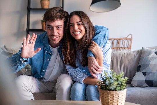 Happy young couple in a video call from home, smiling and sharing joyful news through the laptop or phone camera. Announcing engagement, vacation plans, or exciting updates with friends or family