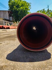A red pipe with a black stripe is laying on the ground. The pipe is long and narrow, and it is...