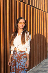 Young woman with acne wearing sunglasses posing by wooden wall