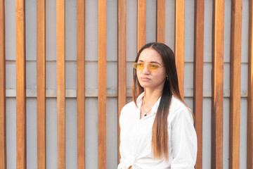 Young woman with acne wearing yellow sunglasses posing in front of wooden wall