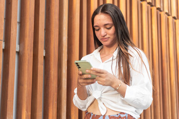 Young latin woman with acne is using smartphone in front of wooden wall