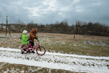 Children enjoying a winter day in a snowy landscape while riding a colorful bicycle along a grassy...