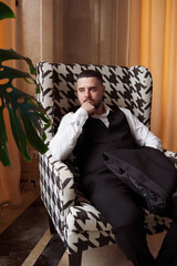 Relaxed stylish man in vest, white shirt and black pants sitting in chair.