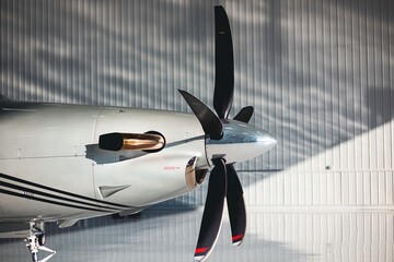 Wide side view of a turboprop aircraft propeller, spinner, and exhaust with reflective hangar wall...