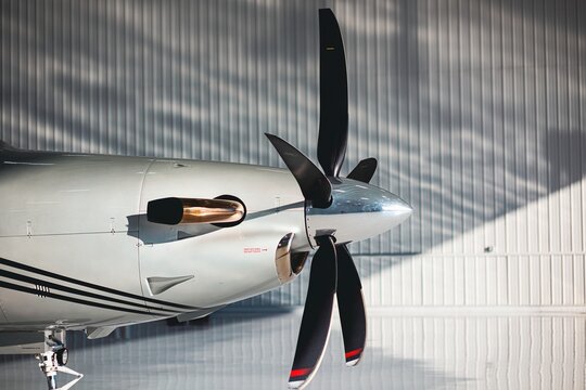 Wide side view of a turboprop aircraft propeller, spinner, and exhaust with reflective hangar wall and natural copy space lighting.