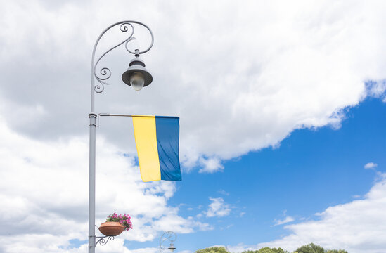 The Ukrainian flag as a symbol of national identity and sovereignty of the country hangs on a lamp post on a city street against the sky. Independence Day, Constitution Day
