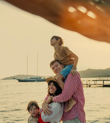 Young happy Caucasian family sitting with two sons on sea pier at sunset, vacation summer travel concept