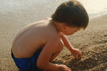 Small child playing with sand on sea beach in summer. Family vacation concept