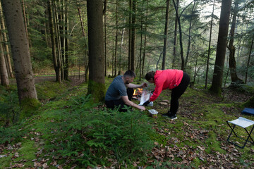 Couple preparing a picnic in a serene forest surrounded by tall trees and lush greenery during a...