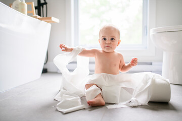Toddler ripping up toilet paper in bathroom