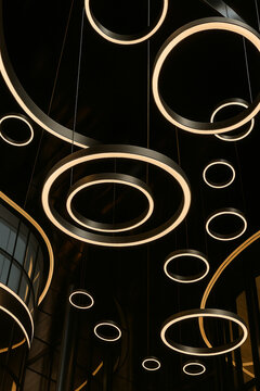 Light ring fixtures hanging from the building ceiling, dark architectural concept photo